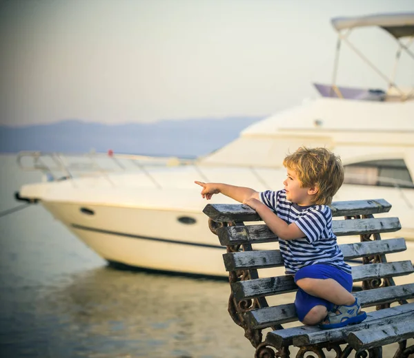 海の港の少年は 船を満たしています 子供の顔に喜び 小さな男の子が海にまで彼の指を指しています うれしそうな新しい経験 ヨットの背景に小さな豊かな船乗り 海の休暇やクルーズ旅行します — ストック写真