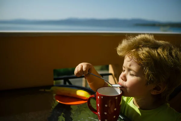 朝食のおいしい牛乳 素敵なかわいい男の子は ドリンクを楽しんでいます 食べることの健康食品 海辺を朝食します バナナ カクテル 乳糖とグルメ 子の美しい顔を照らす太陽 — ストック写真