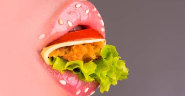 Fast food. Kadın ağız ve burger içinde. Pembe kadın dudakları ile domates, peynir, pirzola ve marul içinde kapatın. Baştan çıkarıcı kadın susam salata tam dudaklarla. Lezzetli ağız