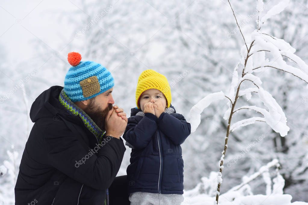 Cold winter. Thermal clothing for children. Funny father and son warm their hands in a frosty forest. Snow and frost. Walk in any weather. Healthy lifestyle. Warm knit hats for a family
