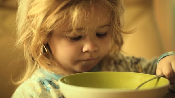 一个漂亮的孩子养活自己 吃牛奶粥 儿童和厨房 健康食品 用勺子和盘子吃早餐男孩 儿童美味的食物 — 图库视频影像