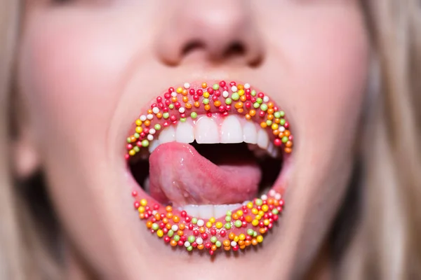 Sweet Lips. Female mouth decorated with candy. Compliments and sweet words. Beautiful mouth of a young girl with creative lipstick. Makeup for a Christmas party. Seductive tongue and white teeth smile