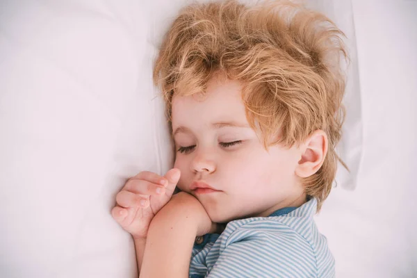 Sweet dreams, sleeping baby with white space pillow. Gentle photo in white tones with cute dreamy boy. Tender baby face, purity and innocence. Healthy child sleep, how to put baby to sleep