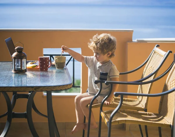 バルコニーで少年朝ココアを飲むとノート パソコン テラスでの休暇 休みの日の朝食 小さな子供には 夏の日が始まります 休日や週末 コーヒーまたは紅茶 — ストック写真