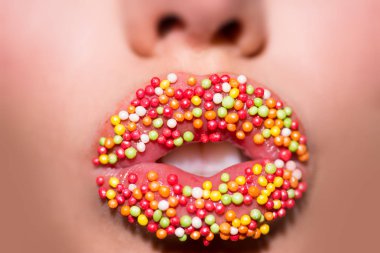 Tatlı dudaklar. Şekerler. Baştan çıkarıcı dudaklar genç kadın renkli tatlı sparckles tarafından dekore edilmiş kapatmak. Güzel dudaklı genç çekici kızdan baştan çıkarma. Tatlı makyaj kadın ağız. Tatlı dükkanı