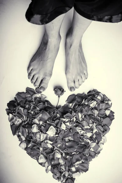 Given love. True love. The heart under the woman's legs. Beautiful concept for Valentine's day. Heart of rose petals before the feet of a young girl. Spa center and female beauty