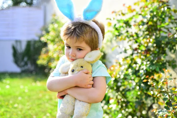 Niedliches kleines Kind mit Hasenohren am Ostertag. Junge mit Spielzeugkaninchen und Umarmung. Liebe und Fürsorge Konzept. Kinder umarmen sich. — Stockfoto