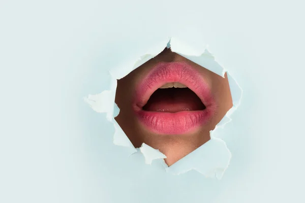 Mouth. Pink lips peep through the hole in the yellow paper. Lipstick, cosmetics, makeup, fashion, beauty.