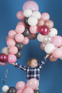 Genç mutlu çocuk yüksek bir mavi arka plan üzerinde uçmak için pembe, gri ve beyaz balon sağlar. Çocuk onun ballons yakalamak için atlar. Tatil, kutlama, yıldönümü için balonlar ve Oyunlar