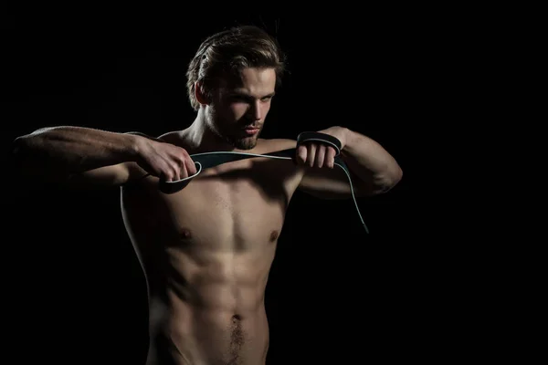 Cinturón en manos de hombre desnudo. El tipo hace ejercicios para las manos con cinturón de cuero. Modelo sexy para accesorios para hombre. Concentración y meditación en el gimnasio — Foto de Stock