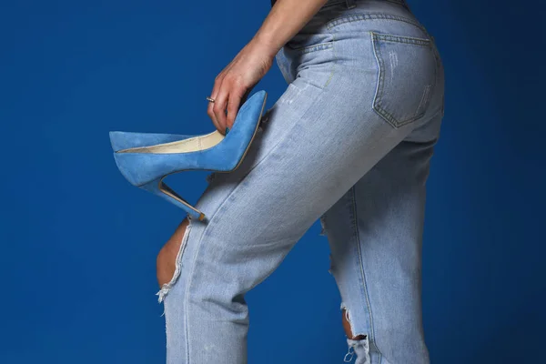 Дизайнер одежды. Женщина держит синие высокие каблуки на ногах. Молодая девушка готовится к прогулке. Изящная девушка в синих тормовых джинсах и голубых каблуках на сером фоне. Подходящие ноги и ягодицы девушки. До даты — стоковое фото