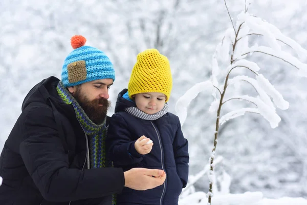 Snowy weather. Caring father calms toddler son outdoors. Boy holding a snowball, wants to share with father, child sincerity and generosity, gentle moments of paternity.