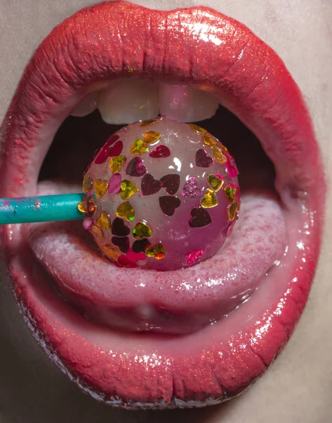 Kvinna slicka lollipop, rosa läppar med lollipop. Sexig kvinna med röda läppar hålla lollipop, skönhet närbild. Godis med hjärtan, söt kyss, avsugning. Karies från socker. Vackra kvinnliga förförisk mun — Stockfoto