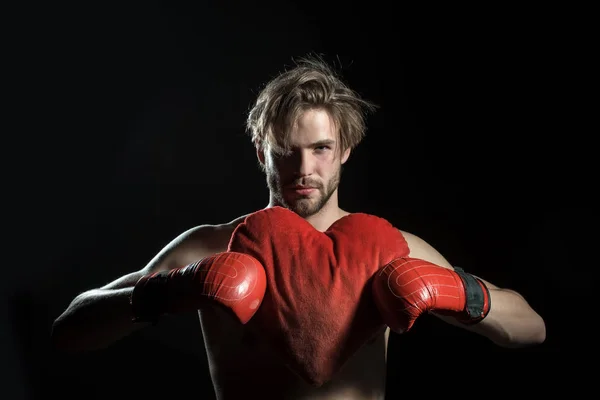 Man in love, broken heart. Boxers heart. Attractive man in boxing red gloves holds heart shaped pillow for St. Valentines Day. In love boxer on black background