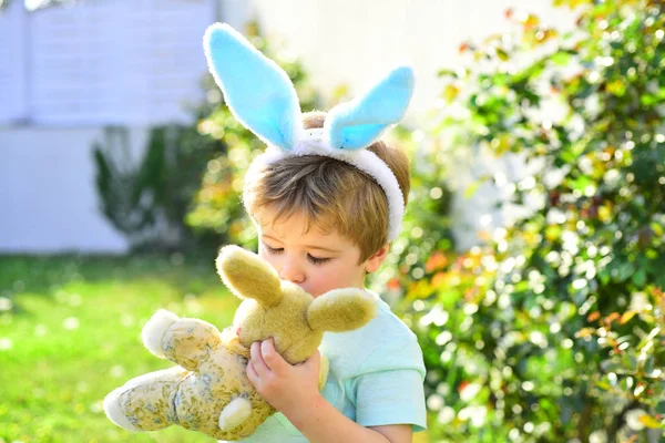 Osterkuss. Kind mit Hasenspielzeug. süßer Junge und sein Spielzeug auf Naturhintergrund — Stockfoto