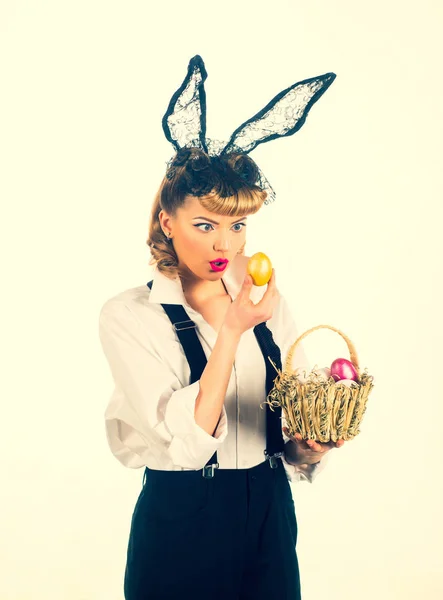 Easter eggs concept. Surprised woman looks at the golden egg. Discounts sales for Easter. Emotional girl with bunny ears.