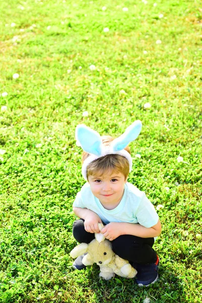 Baby im Hut wie ein Hase mit Bärenspielzeug auf grünem Gras im Freien. Osterferien. — Stockfoto