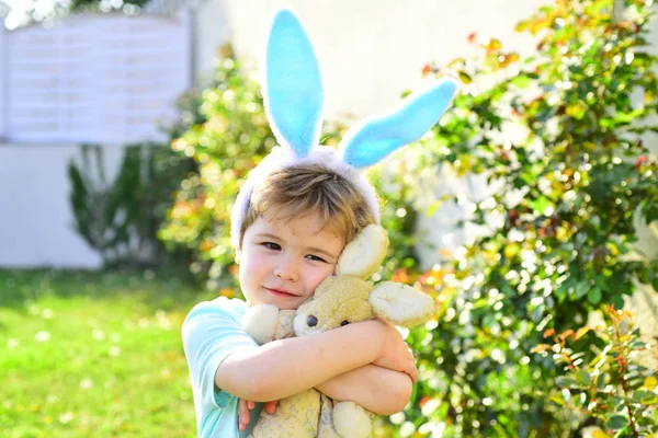 Niedliches Kind mit Hasenohren an der frischen Luft hält und umarmt sein Hasenspielzeug. aufrichtige, reine Emotionen vom Kleinkind an auf natürlichem Hintergrund. Familienruhe auf dem Land. Freundschaft zwischen Kind und Tier. Zoo — Stockfoto