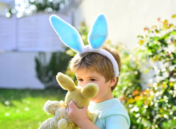 Rabbit kid. Cute boy with blue bunny ears tries to kiss little rabbit to show love. Sincere emotion from child in garden. Games outside for children. Moment captured during Easter day. Child costume
