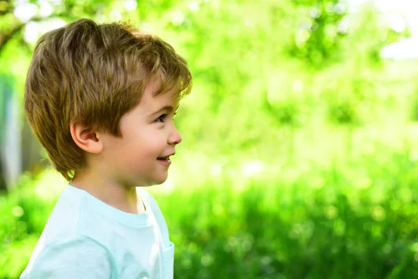 Lindo chico sonriente mira algo. Paseo familiar en el jardín durante el cálido día soleado. Vacaciones familiares con niños en el campo. Fondo natural verde durante el verano — Foto de Stock