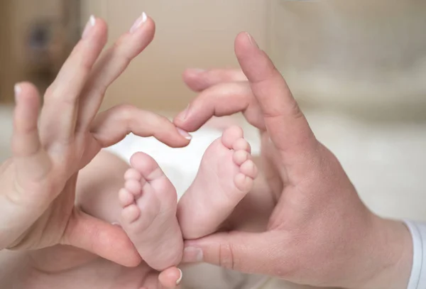 Pés de bebé recém-nascidos em mãos de mãe, em forma de coração adorável. Mãe e pai segurando pernas da criança em mãos. Imagem de perto. Conceito de família feliz — Fotografia de Stock