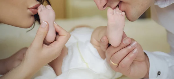 Amor familiar, beijo suave para recém-nascido. Mãe e pai seguram pés de bebê pernas em suas mãos e beijá-los. Amor recém-nascido e parental. Pais felizes após o parto . — Fotografia de Stock