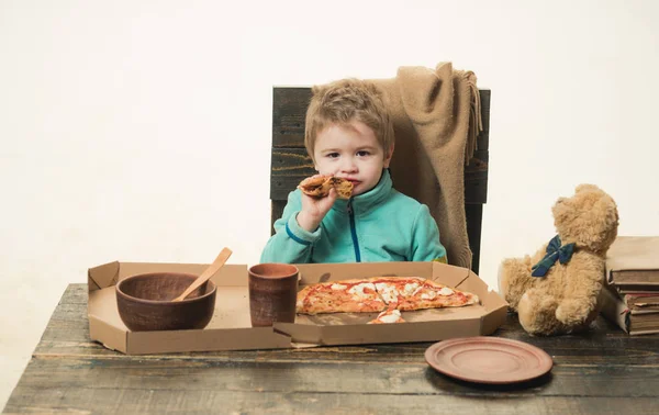 子供は白い背景に孤立した木製のテーブルでピザを食べます。イタリアの自家製素朴な食べ物。クマのおもちゃで男の子のランチ。グルテン料理。就学前の子供のためのおいしい料理。夕食とファストフード — ストック写真