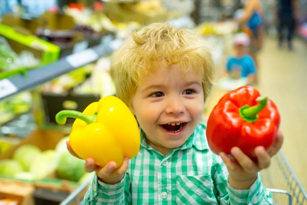 健康的なライフスタイル。スーパーマーケットで愛らしい小さな男の子は彼の誠実に幸せな感情を示しています。子供は店でコショウで遊ぶ。スーパーマーケットでショッピングカートでかわいい子供の歓声。家族と一緒にショッピング — ストック写真