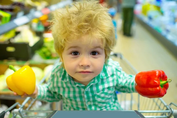 春のショッピング、野菜の購入。野菜や健康的な食品の店でクールな面白い顔をしてかわいい子供。美しい家族、子供の顔は、カメラを見ています。夕食には黄色と赤のコショウ — ストック写真