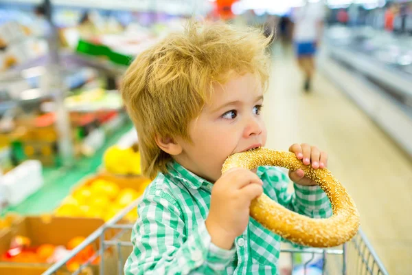 L'appétit du bébé. Nourriture pour enfants. Un enfant mange un chignon avec de la graine de sésame. Supermarché et pâtisserie. Du pain frais. Délicieux petit déjeuner. De la nourriture pour bébé. Beau gosse avec de la nourriture au magasin. Portrait d'enfant — Photo