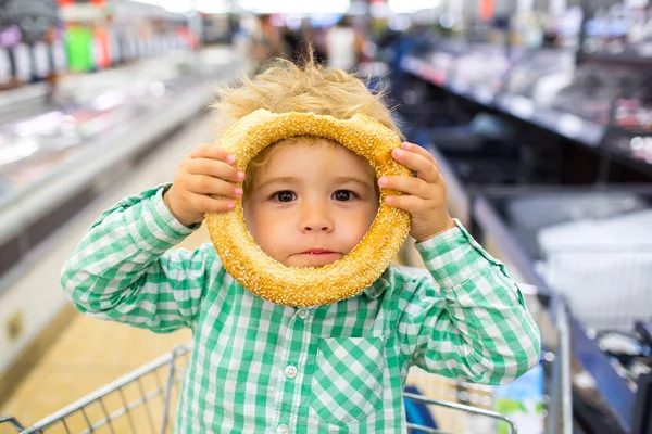 Enfant heureux avec un pain savoureux. Menu pour enfants. Enfant émotionnel actif avec une collation rapide. Drôle de shopping avec les enfants. Drôle de garçon au supermarché jouant avec un chignon rond. Menu sans gluten . — Photo