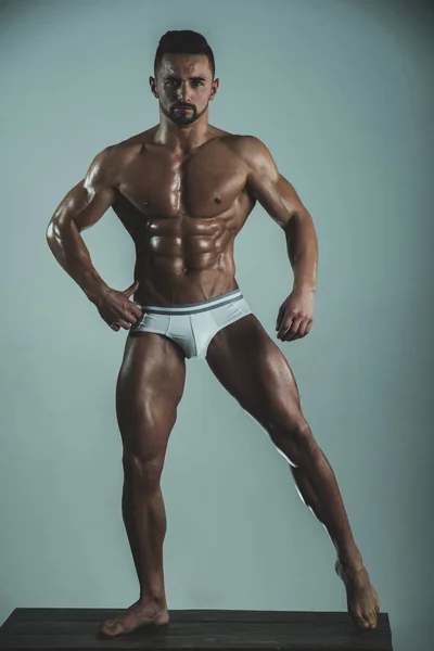 Macho chaud montre son corps musclé. Les muscles séduisants du jeune homme. Corps bien entraîné. Corps, torse et pression parfaits. Barbu élégant jeune homme sur fond gris. Compétition fitness . — Photo