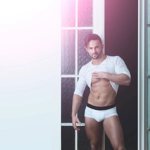 A man in white underwear. Mens fashion. Homewear. Young guy in a white T-shirt. Husband or groom. Lover.