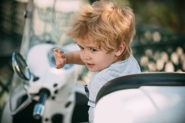 Coche de niños. Pequeño conductor. Bebé de vacaciones. Entretenimiento de fin de semana. El chico detrás del volante agitando una mano a la cámara. Chico feliz. Tiempo en familia . — Foto de Stock