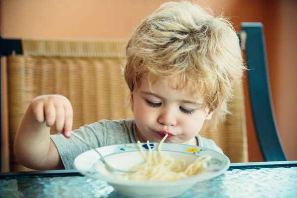 おいしい麺を食べる子供、インドの子供は自宅でフォークとスパゲッティを食べます。小さな男の子がフォークでスパゲッティを食べている。テーブルの上に座ってスパゲッティを食べる愛らしい小さな男の子の子供 — ストック写真