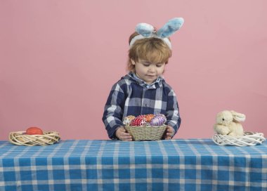 Paskalya yumurtası avı olan çocuk. Evde renkli yumurta arayan tavşan kulakları ile çocuk. Tavşan kostümlü toddler erkek okul öncesi kız kapalı oyun. Güzel bebek yumurta ile bir Paskalya sepeti tutan