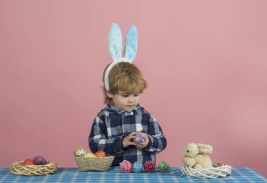 Çocuk Paskalya dekore mor yumurta tutar ve masada kabarık bir tavşan bakar. Paskalya yumurtaları küçük çocuk tarafından hazırlanır. Çocuklar ve ebeveynleri için gelişim hobileri. Sevimli Paskalya konsepti arka plan