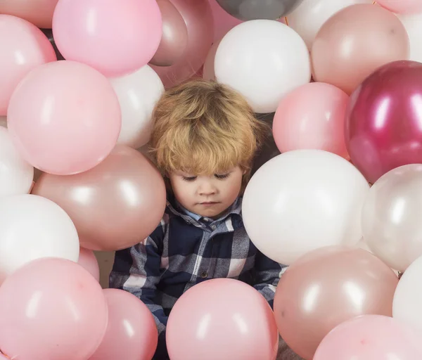 Child in balloons. Birthday party. Tired child after holiday. Celebrity life. Pink balloons and sad kid boy. Lonely child without parents is sad and frustrated. Cute baby close up, pink background
