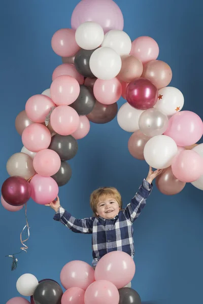 Little kid holds ballon arch above his head on blue background. Background. Child and arch. Happy emotions from cheerful kid with ballons. Simple decorations childrens celebrations