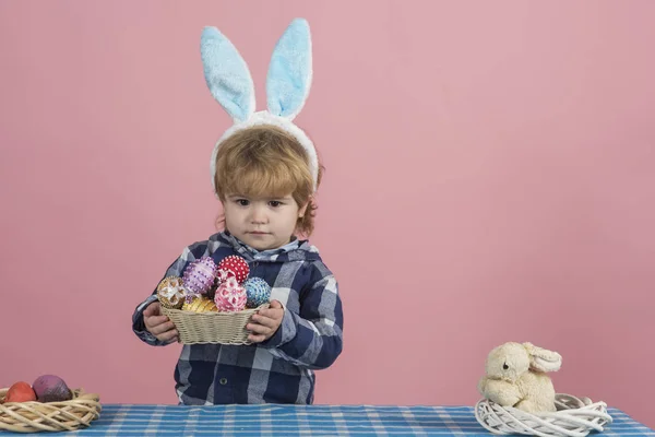 Wielkanoc prezent od cute Kid w puszyste uszy króliczka. Dziecko na różowym tle. Koncepcja Wielkanocna. Mały chłopiec w niebieskiej koszulce posiada miskę ze słomy pełnej pisanek na różowym tle — Zdjęcie stockowe