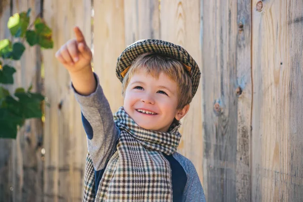 Il ragazzo sorride e mostra il dito in su. Promozione e vendita. Faccia da bambino. Pubblicità per bambini. Bambino in sciarpa su uno sfondo di legno . — Foto Stock