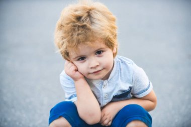 Çocuk yorgun. Yakışıklı bir çocuk çömeldi ve eliyle başını destekledi. Aktif çocuk. Maçtan sonra dinlen. Akıllı bebek bakışı. Mutlu çocukluk konsepti.