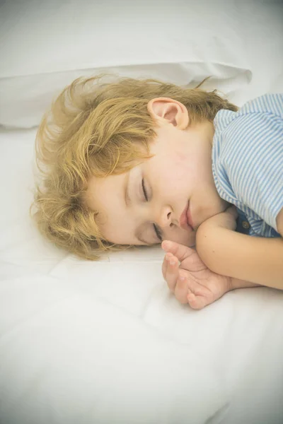 Adorable little boy sleeping in bed. Child is taking a nap. Sleeping in bed little boy. Child sleeping and dreaming in his bed. Linens. Sweet dream.