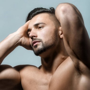 Mavi arka plan üzerinde güçlü kaslı vücut ile yakışıklı adam Portresi. Erkek vücut ve görünüm moda trendi. Modern sakal ve saç kesimi ile Esmer bodubuilder. Striptiz kavramı.