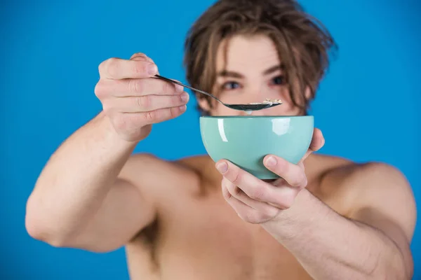 Desayuno saludable. Hombre sexy desnudo come avena gachas de avena de un plato azul. Deliciosa comida, cubiertos y hermosos platos en la cocina. El hombre preparó el desayuno para su mujer. — Foto de Stock