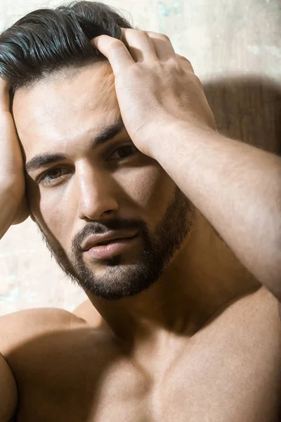 Sexual muscular nude man posing over white background. Man has headache, he holds his hands on head. Medecine from pain, painkillers. Sensual portrait of handsome guys face. Trendy haircut.