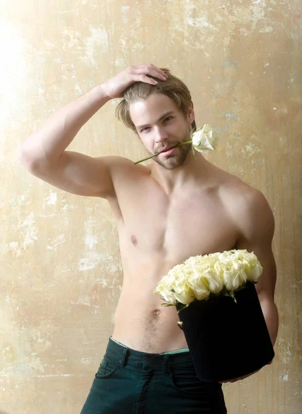 Hombre con ramo de rosas. Sexy chico guapo semidesnudo toca el pelo. Bonito cuerpo y flores encantadoras. Postura seductora con flor en los dientes — Foto de Stock