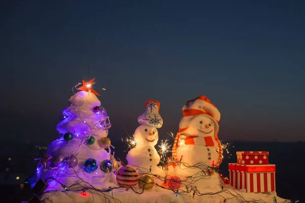 Humor de Navidad, muñecos de nieve saludan a Santa Claus. Un nuevo año en las montañas. Sombrero de Navidad y bufanda. Decoraciones para Navidad y Año Nuevo. Estrella, bolas y garlande en el árbol de navidad. Celebraciones de invierno — Foto de Stock