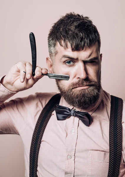 Man with beard and mustache holds straight razor. Hairdresser in stylish shirt demonstrate sharp blade dangerous razor. Bearded hairdresser with straight razor for shaving.