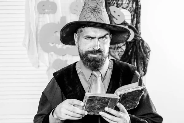 Scary man with a book of magic. Bearded wizard. Halloween hero. The guy in the costume for the magical party. Best father ever. Spiderweb and pumpkin on halloween background.